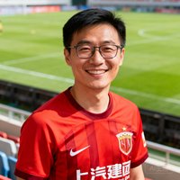 一位戴眼镜的中国男性球迷张磊，穿着红色球衣，面带微笑站在球场看台前，背景是模糊的绿茵场。